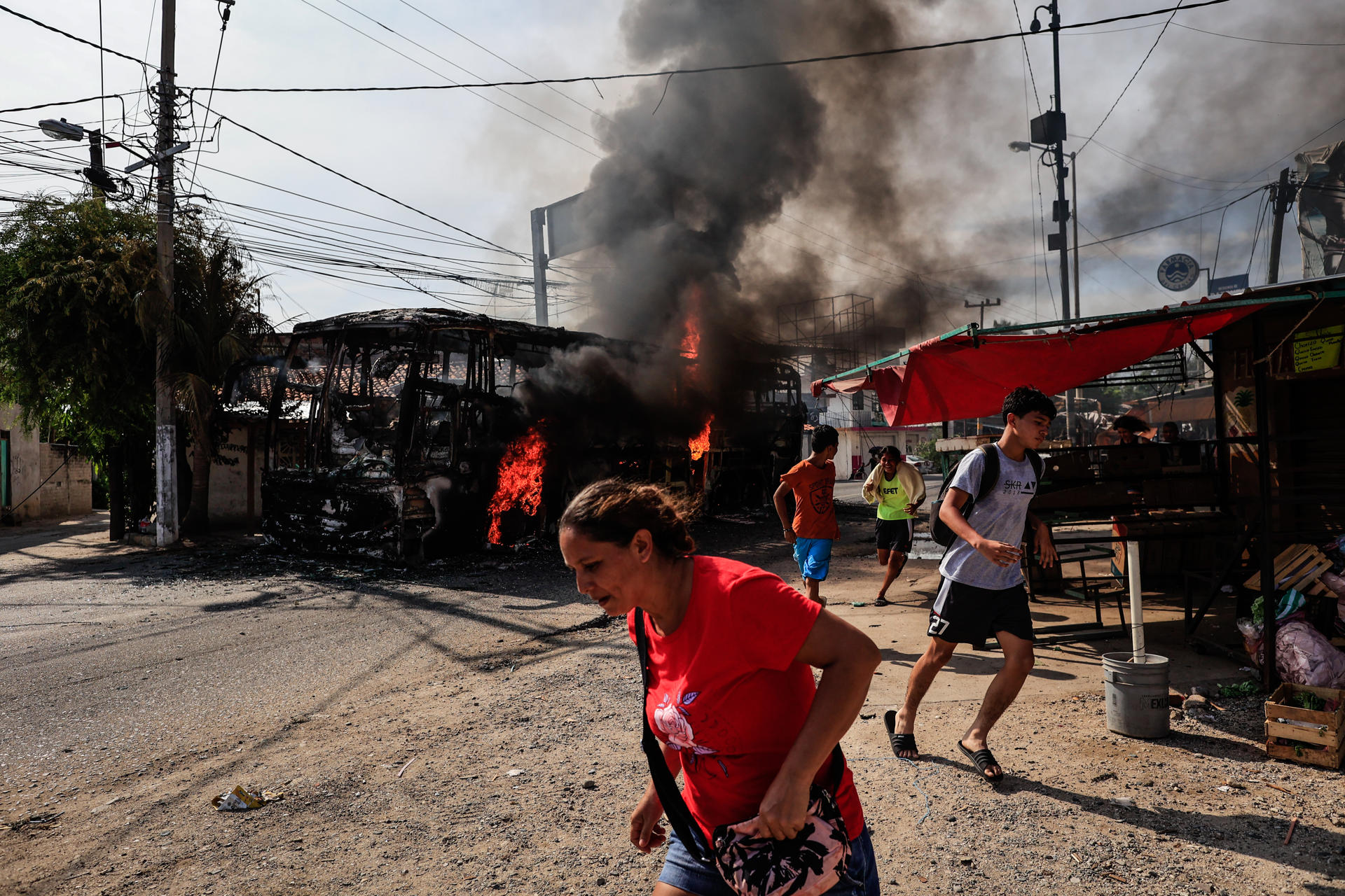 Personas corren al lado de un camión que fue incendiado hoy, en el balneario de Acapulco, estado de Guerrero (México). EFE/David Guzmán.