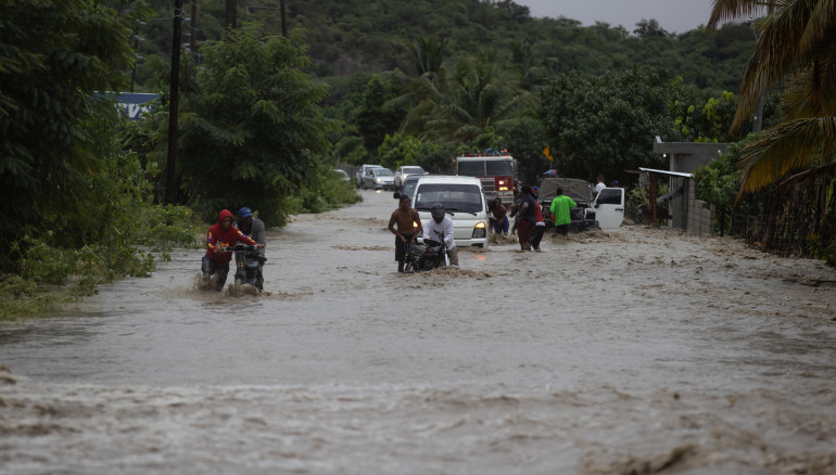 Personas cruzan con dificultad la carretera que se encuentra inundada producto de las intensas lluvias, hoy en San José de Ocoa (República Dominicana) /EFE/Orlando Barría.