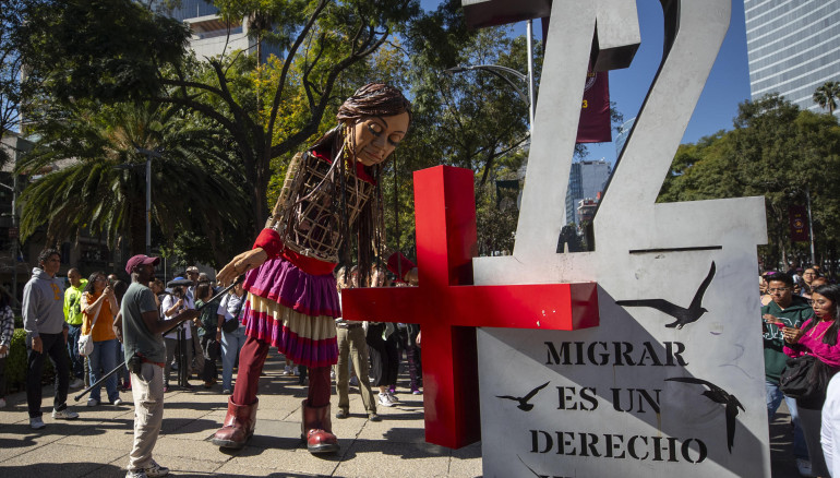 La marioneta Amal, que representa a una niña migrante siria, saluda a las personas durante su recorrido hoy, en la Glorieta de la Diana, a la Glorieta de los Desaparecidos, en avenida Paseo de la Reforma, en la Ciudad de México. EFE/ Isaac Esquivel